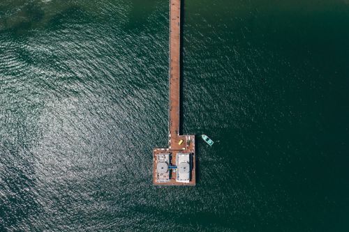 Free Drone view of a wooden dock stretching into the water with a boat nearby, creating a serene scene. Stock Photo