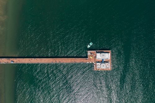 Free Stunning aerial view of a dock stretching into the ocean with a small boat moored nearby. Stock Photo