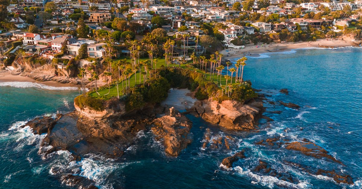 Stunning aerial view of Laguna Beach with rocky coastline, palm trees, and ocean waves.