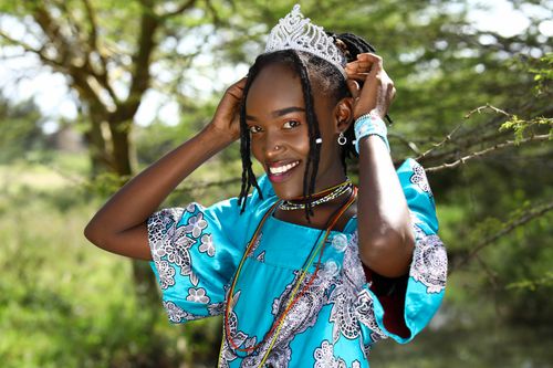 Free A beautifully adorned woman in a blue dress and tiara poses joyfully in a natural setting. Stock Photo