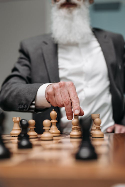 A Person in Black Suit Jacket Holding Brown Wooden Chess Piece