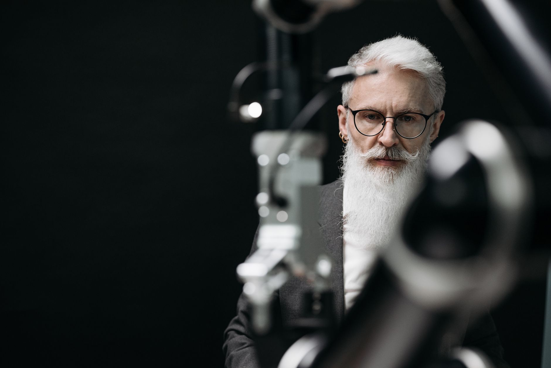 Senior man with white beard and eyeglasses looking intensely, set against a blurred backdrop.