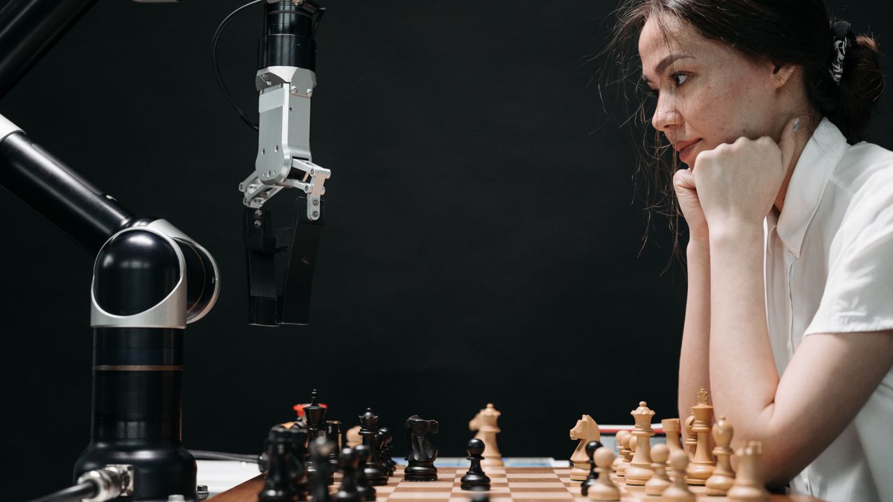 Woman strategizing a chess game against a robot arm, illustrating technology and strategy.