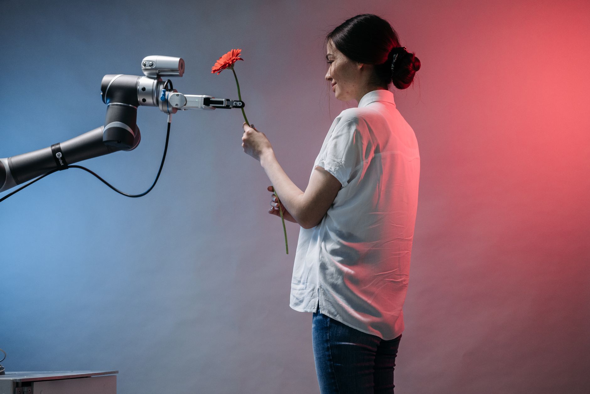 A woman interacts with a robotic arm holding a flower, showcasing technology and human connection.