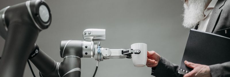 An elderly man receives a cup from a robotic arm in a modern office setting.