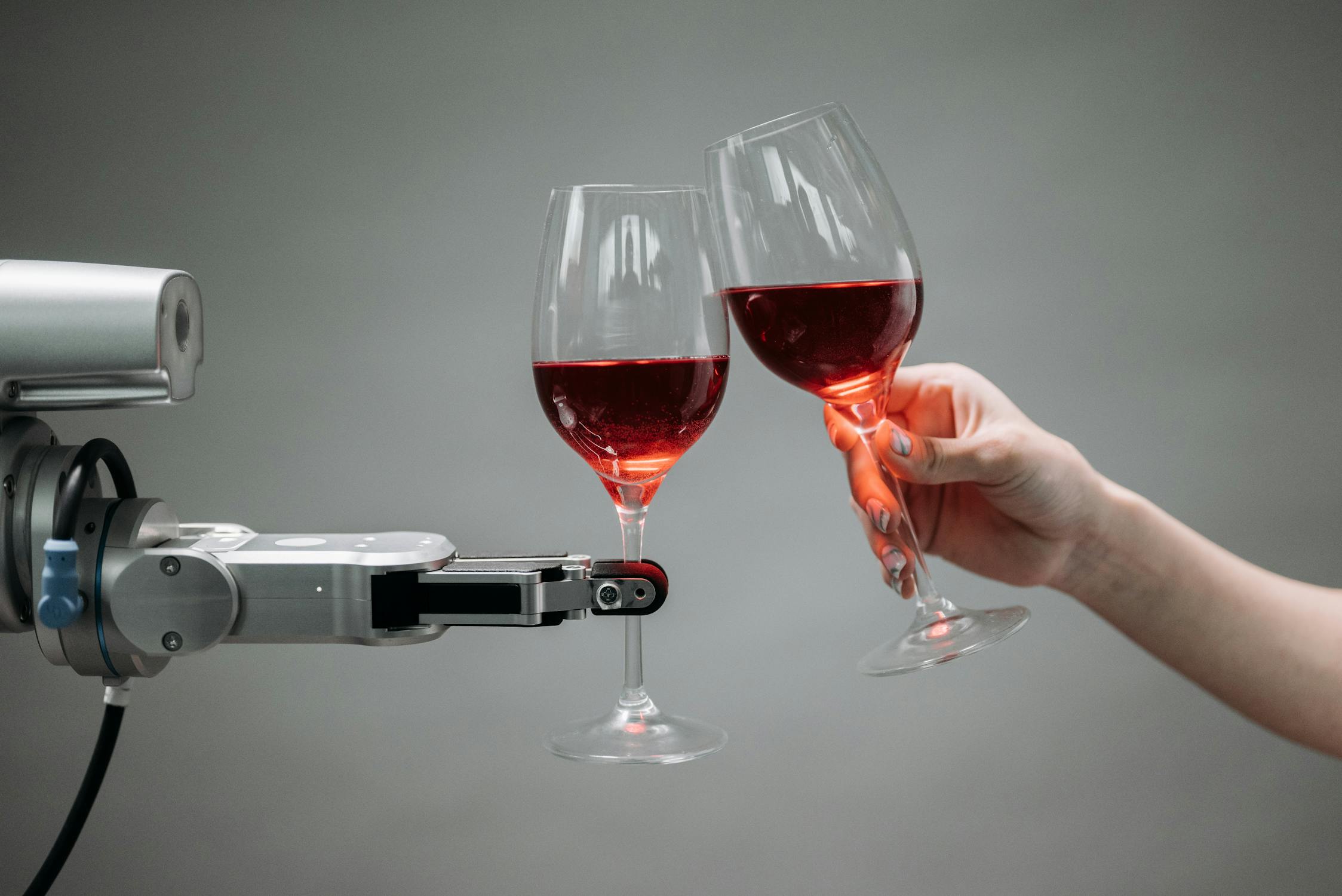 A robot arm holding a wine glass and toasting with a human hand holding a wine glass