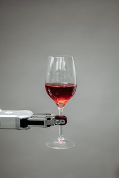 Close-up of a robotic arm holding a glass of red wine against a gray backdrop, showcasing technology and innovation.
