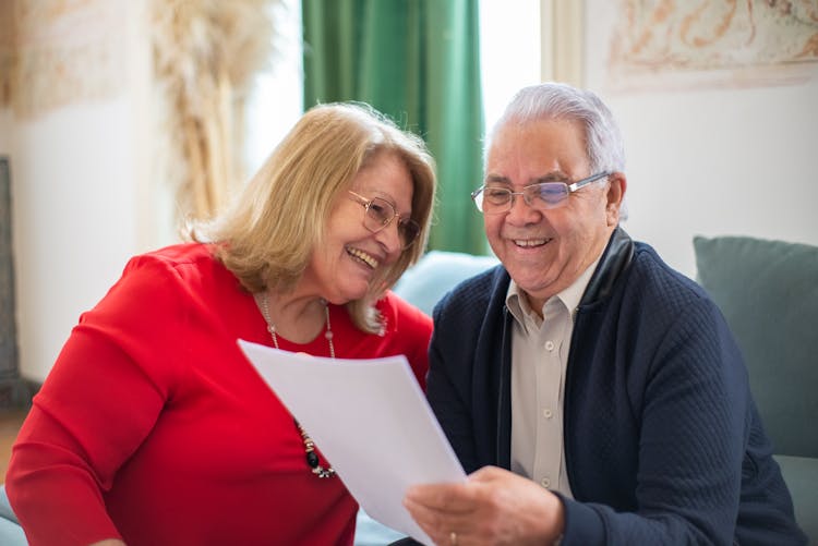 Smiling Couple Reading A Paper And Sitting On A Couch