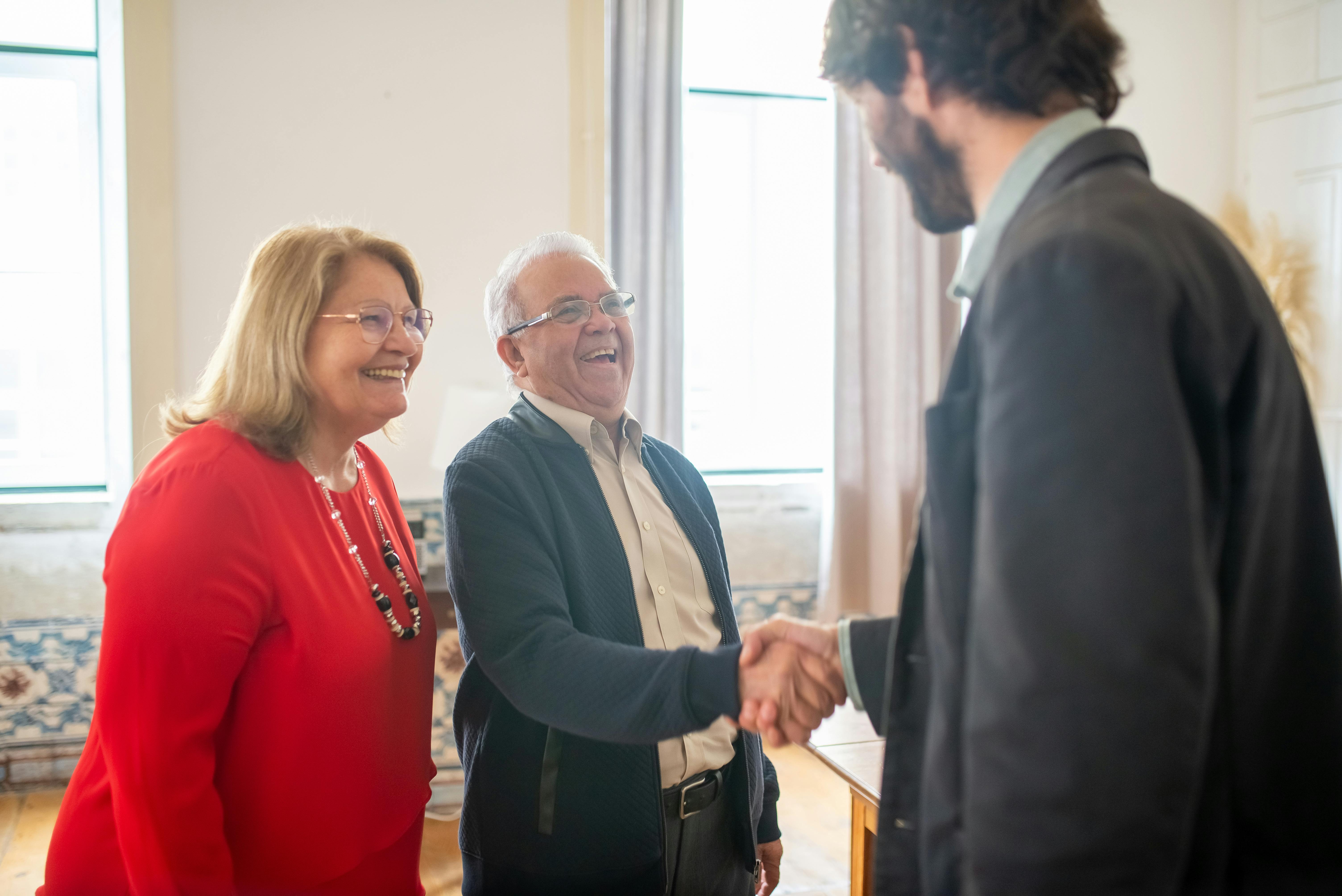 Senior couple meeting a professional in a bright indoor office setting, exchanging smiles and a handshake.