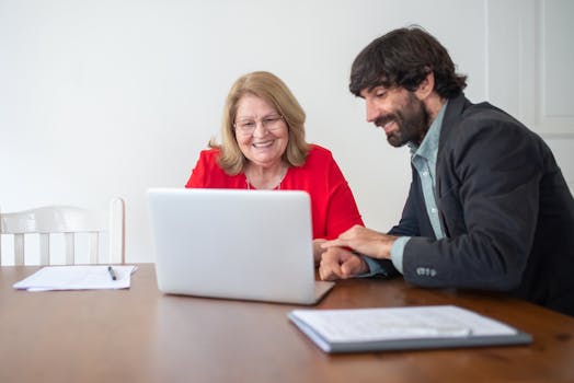 Smiling elderly woman and man working on a laptop indoors, showcasing teamwork and learning.