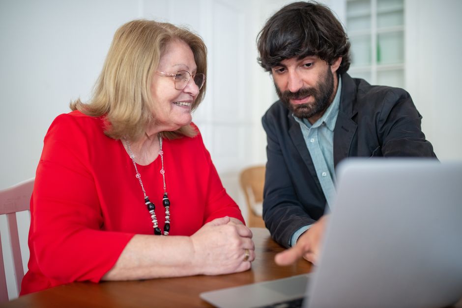 A man and senior woman discuss work on a laptop indoors, focusing on technology and consulting.