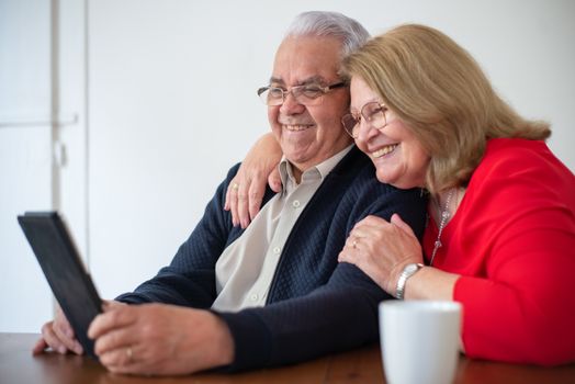 Happy senior couple embracing while using a tablet indoors. Perfect for technology and lifestyle themes.