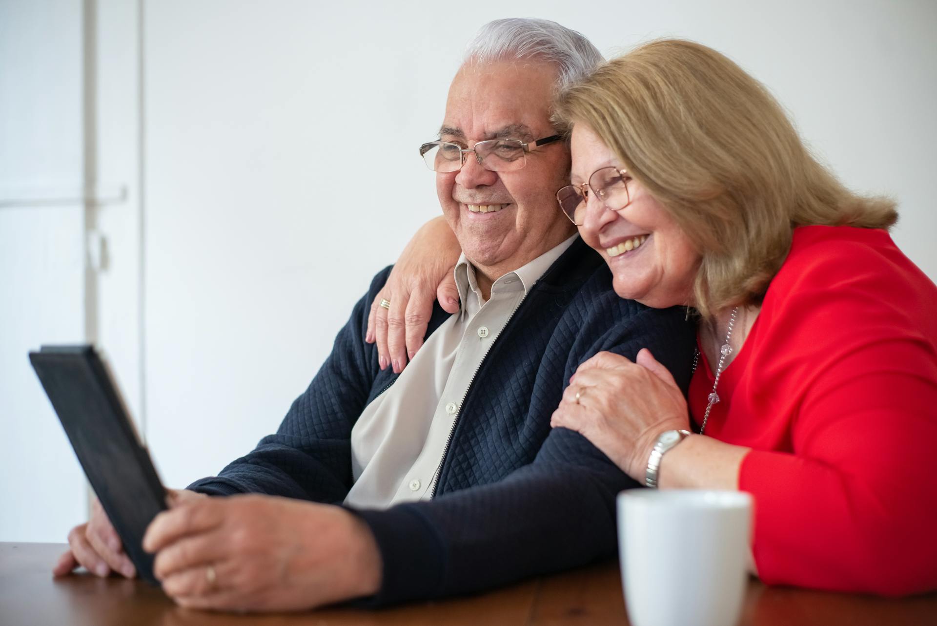 Happy senior couple embracing while using a tablet indoors. Perfect for technology and lifestyle themes.