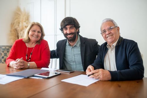 Free Group portrait of two senior adults and a young man smiling at a business meeting indoors. Stock Photo