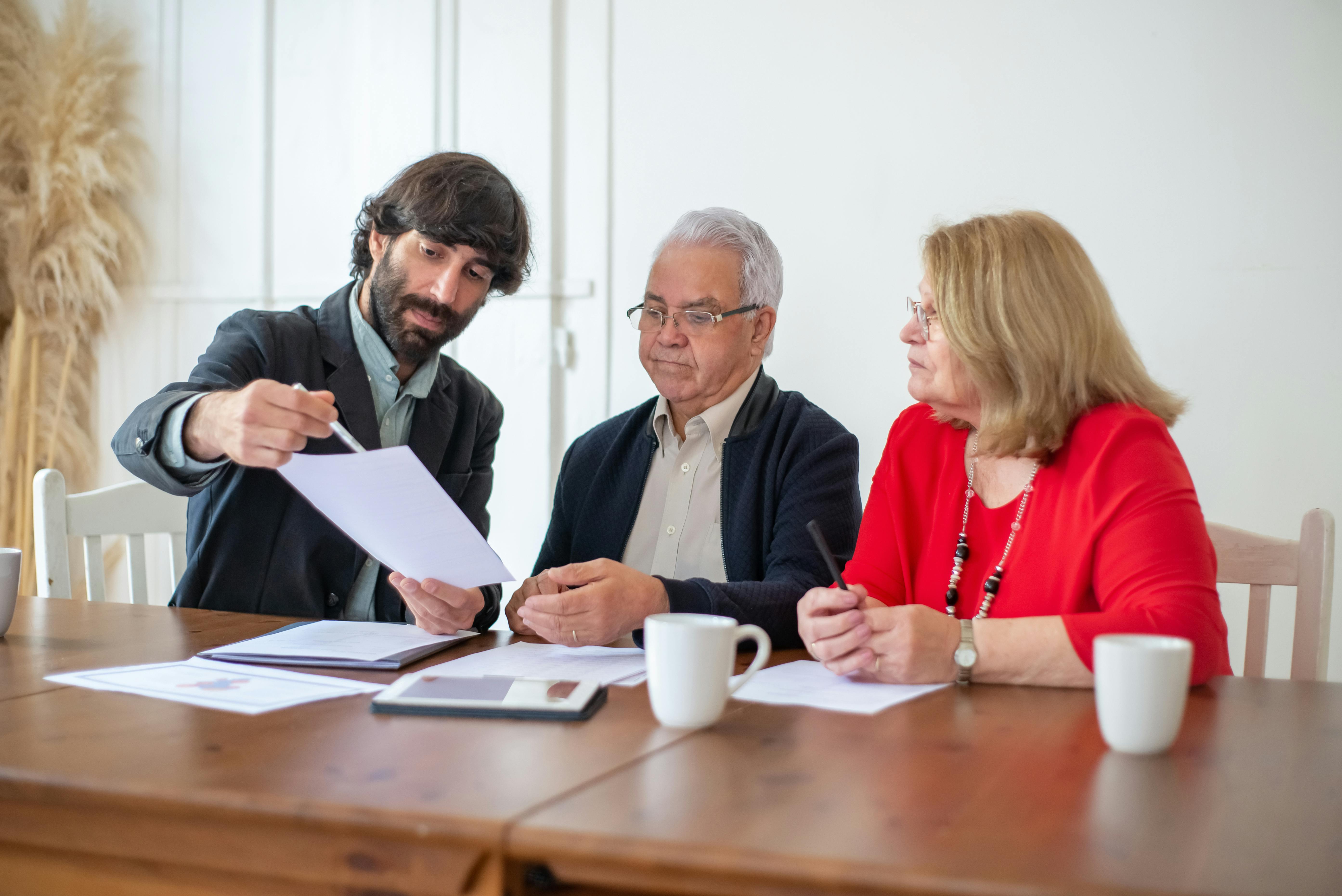 bearded man showing papers to a couple sitting at the table