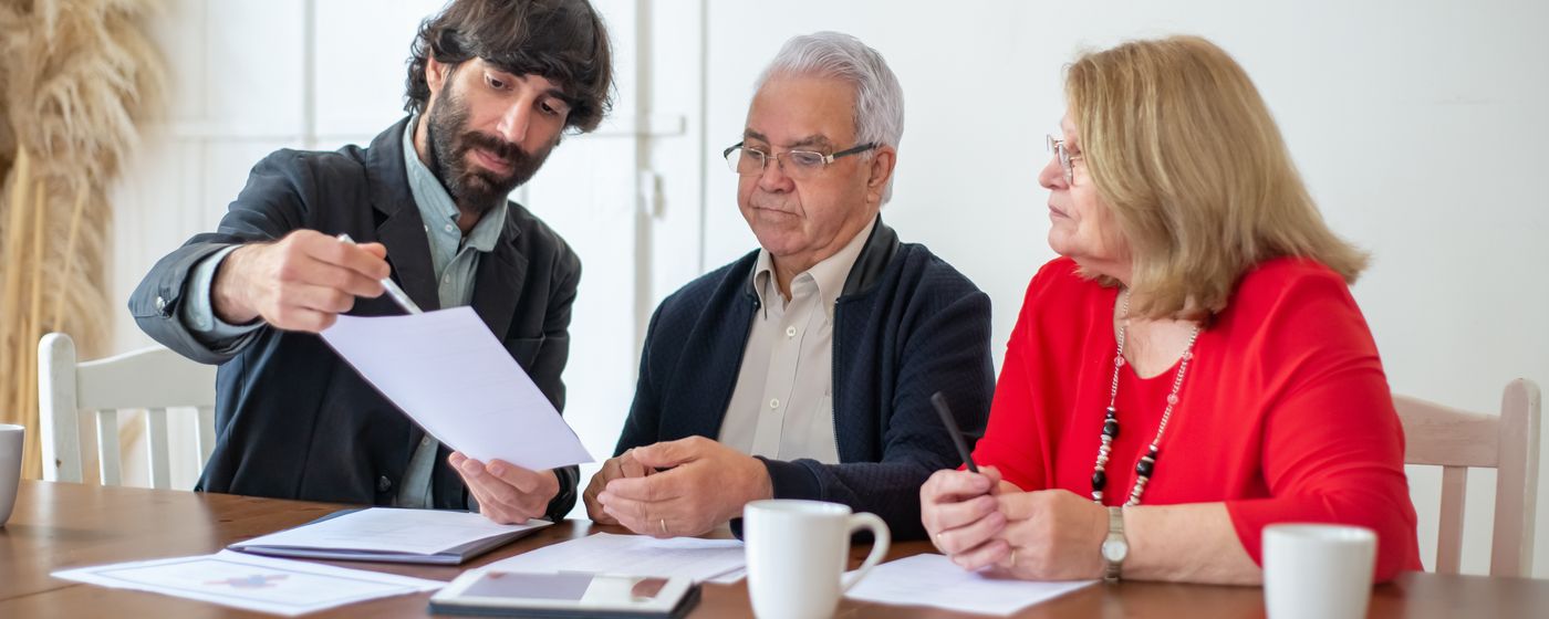 Adviseur bespreekt documenten met een ouder echtpaar aan een houten tafel