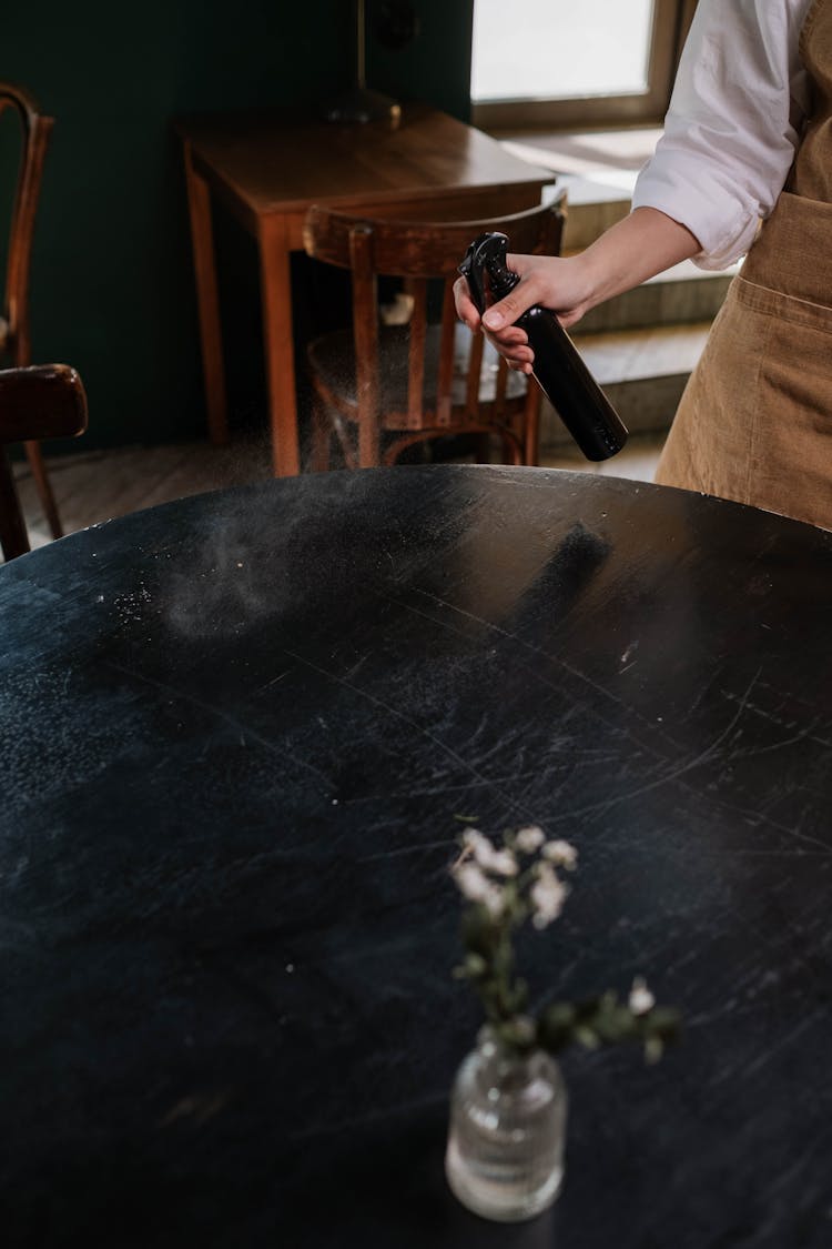 Person Holding Black Spray Bottle And Cleaning Black Round Table