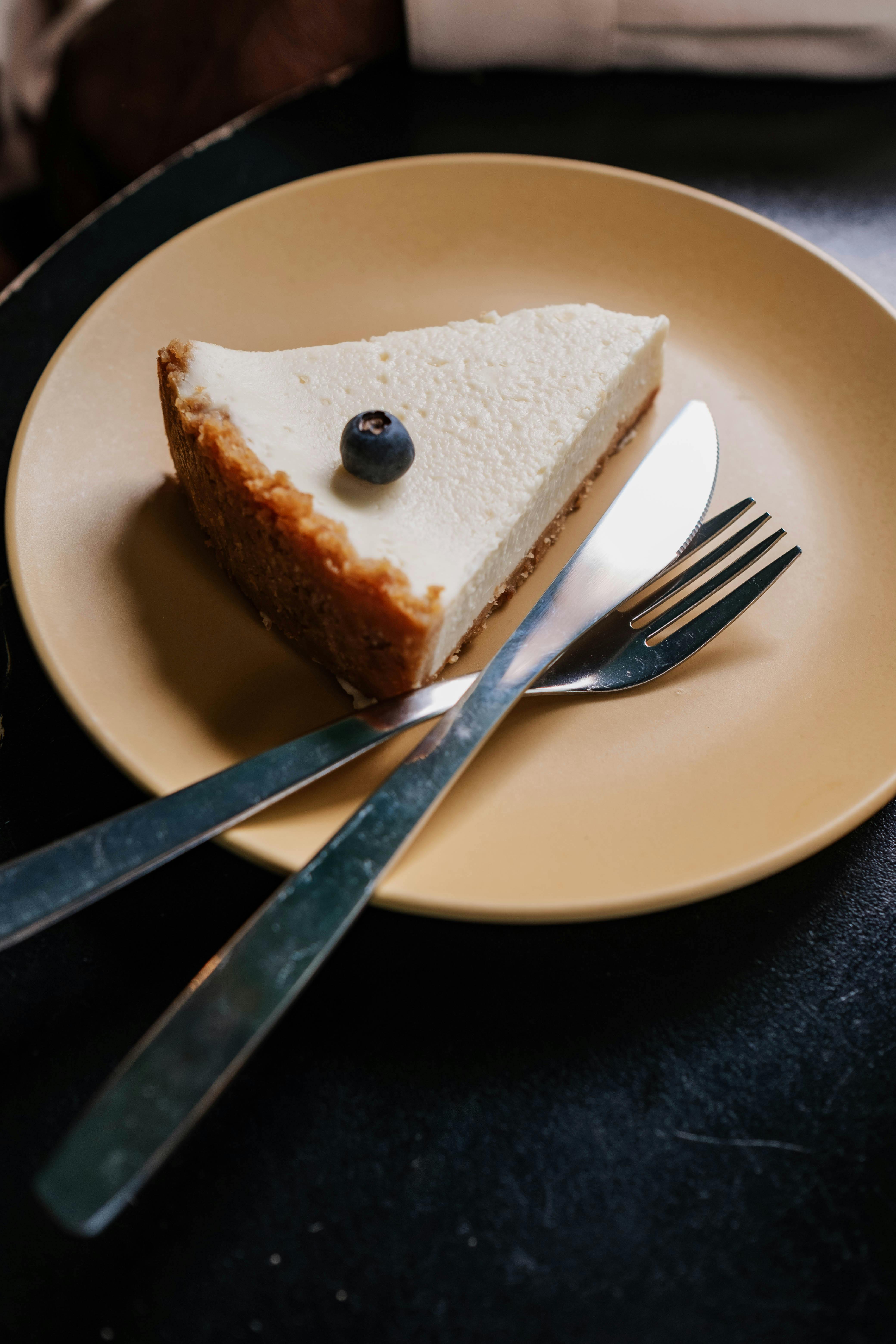Close-up of a slice of cheesecake with blueberry on top, served on a plate.