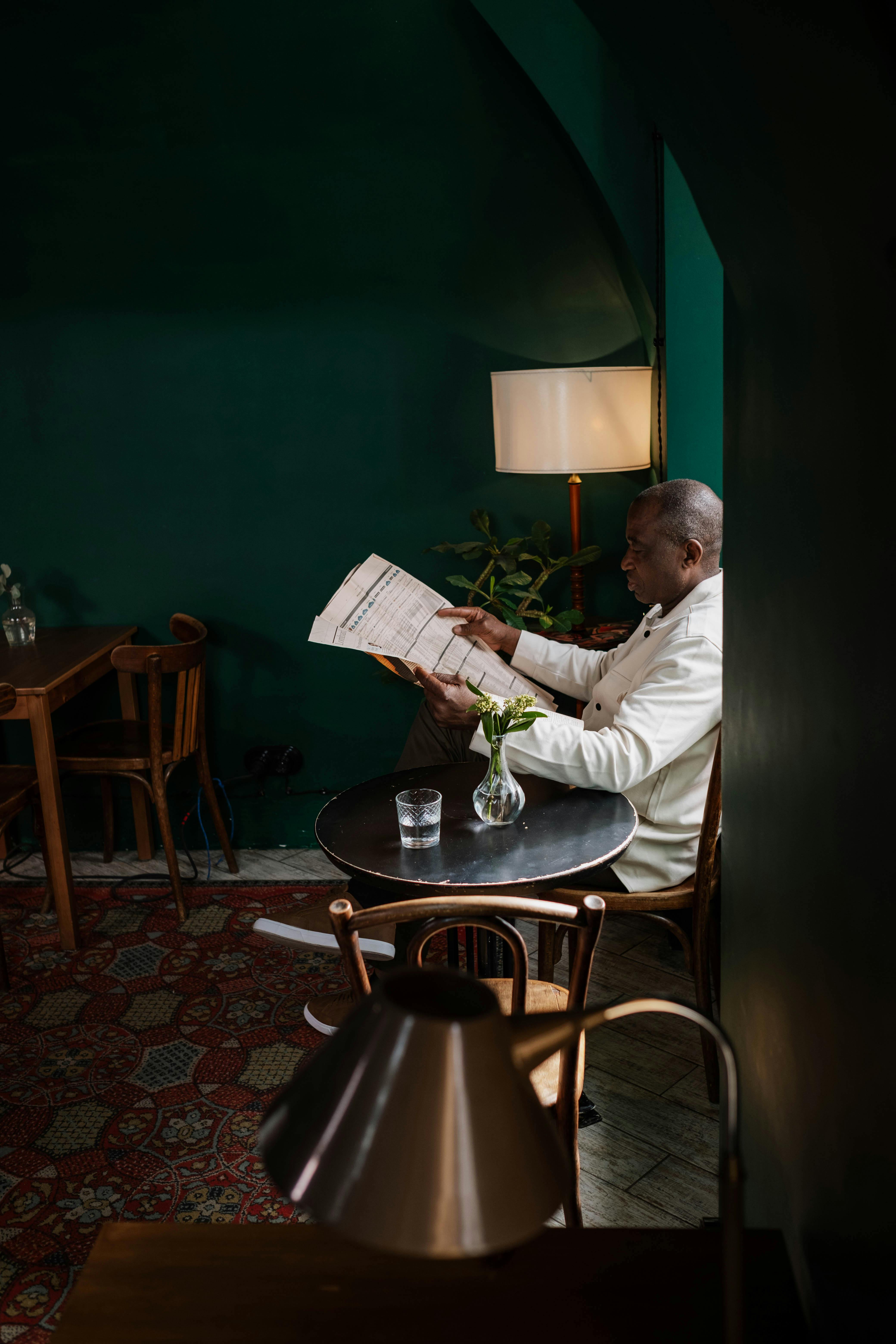 African American man reading a newspaper in a quiet, warmly lit café setting.