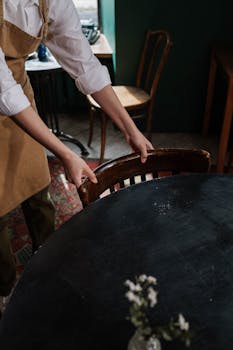 A waitress arranges a chair in a cozy, rustic café setting, emphasizing a warm atmosphere.