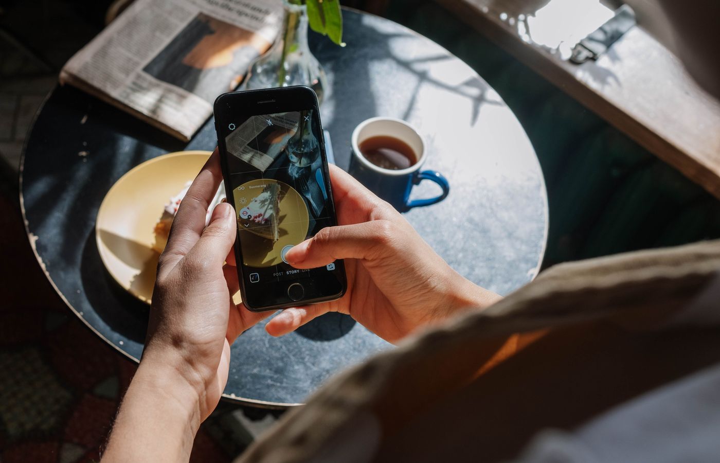 Hands capturing a cake and coffee setup in a cozy cafe environment.