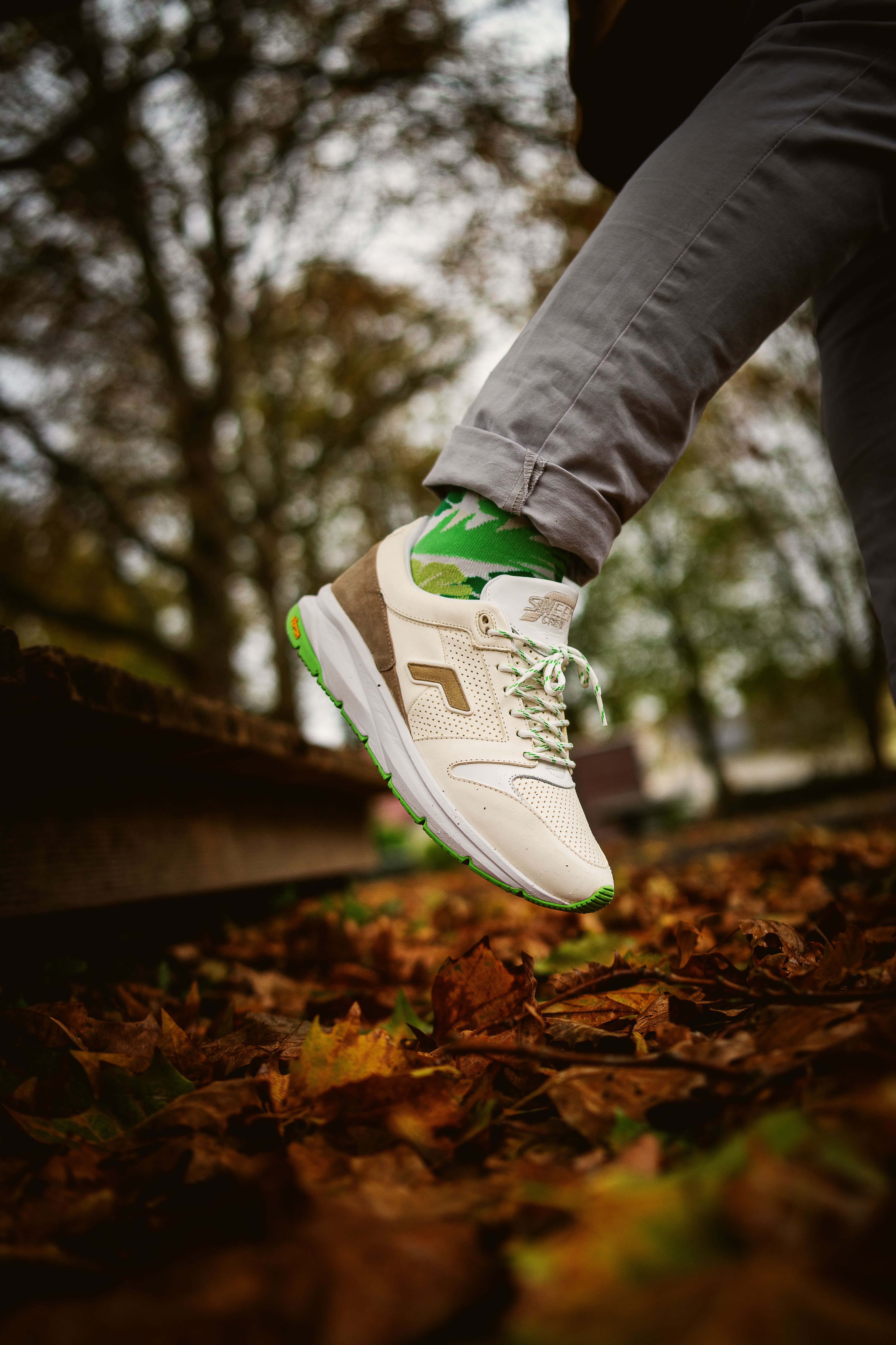 Stylish sneaker stepping through colorful autumn leaves in a blurred forest background.