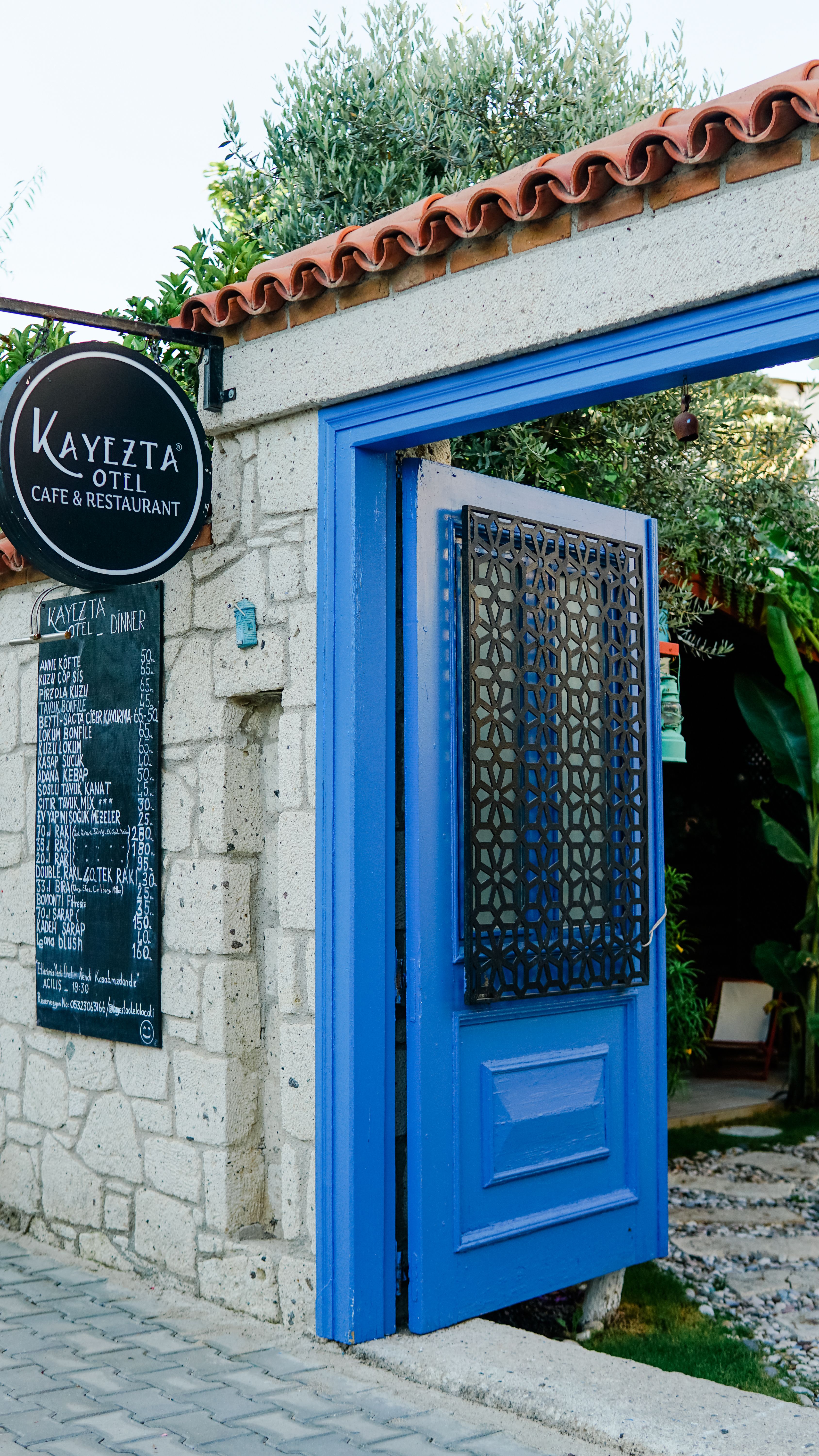 Open blue door at Kayezta Hotel, a quaint café in Alaçatı, İzmir, Türkiye.