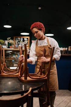 Waitress arranging chairs in a cozy café setting, preparing the space.
