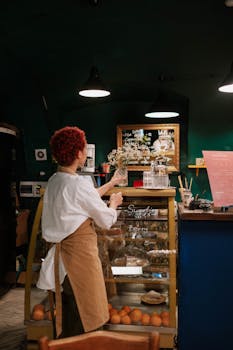 A waitress with short hair organizes a display in a cozy café. Indoor warm lighting.