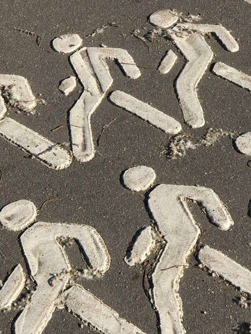 Free Close-up of white pedestrian symbols on a rough asphalt city pathway. Stock Photo