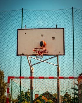 Basketball going through hoop on an outdoor court with a net backdrop, captured in action.