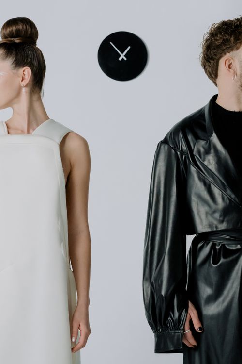 Free A man and woman in modern attire stand apart in a studio with a clock on the wall, captured in a minimalist style. Stock Photo