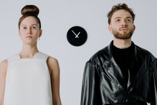 Stylish portrait of a man and woman in fashionable outfits against a minimalist white background.