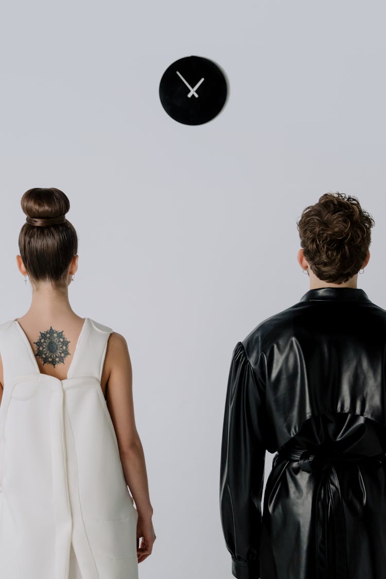 Woman And Man In Black And White Costumes Looking At A Clock On The Wall 