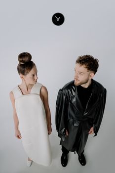 Minimalist portrait of man and woman in stylish outfits with a conceptual clock background.