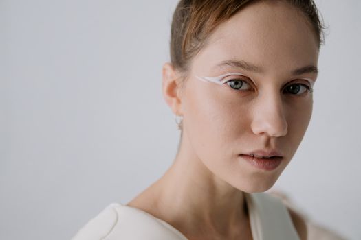 Close-up portrait of a woman with unique white eye makeup and minimalist background.