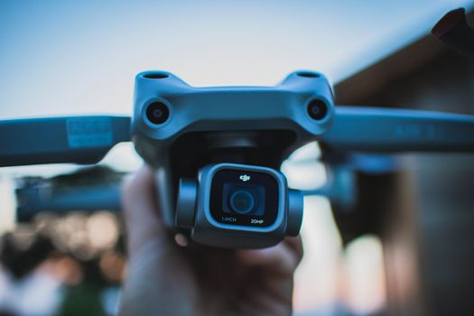 Detailed close-up of a hand holding a drone camera with blurry background, captured outdoors.
