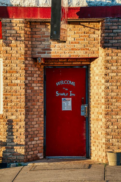 Free Red door of Stumble Inn in Millville, MN, with a welcoming sign and brick facade. Stock Photo