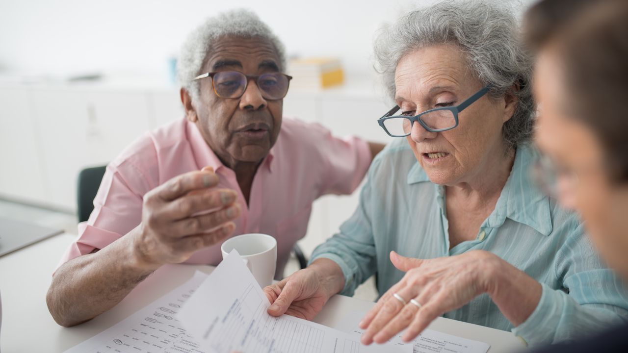 Elderly couple discussing financial documents with a consultant in an office setting.