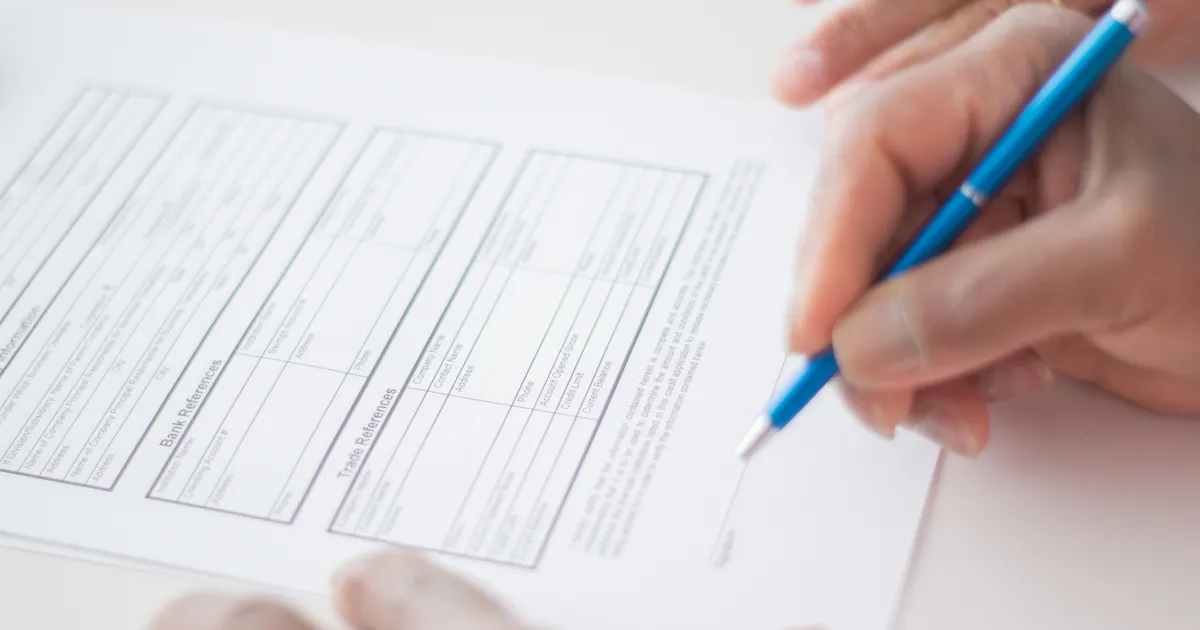 A hand filling out a printed form with a blue pen, representing Texas TRAIGA compliance checklist 2026