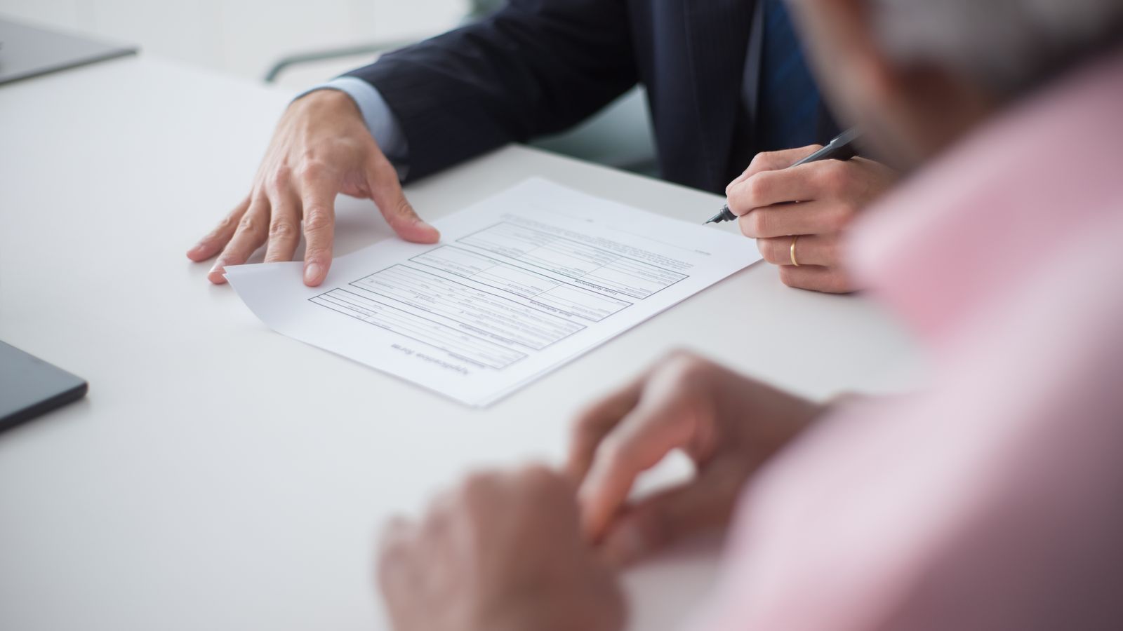 Deux professionnels signant des documents lors d'une réunion de travail autour d'une table.