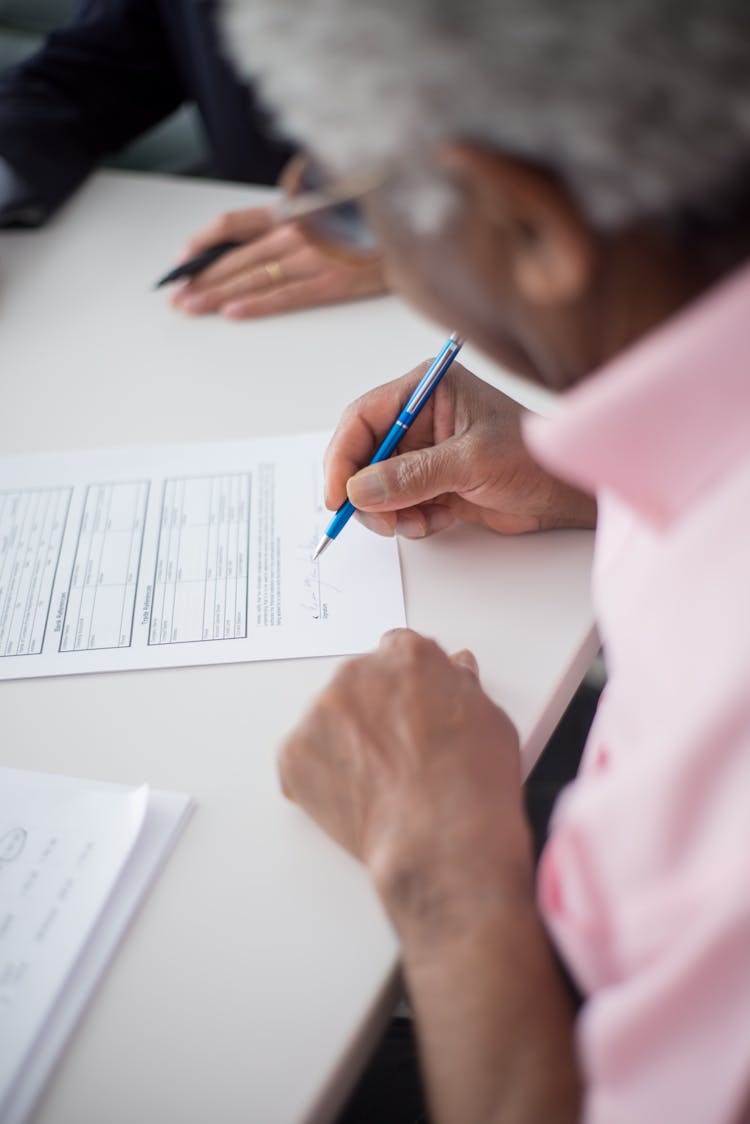 A Person In Pink Polo Holding A Pen While Looking At The Document On The Table