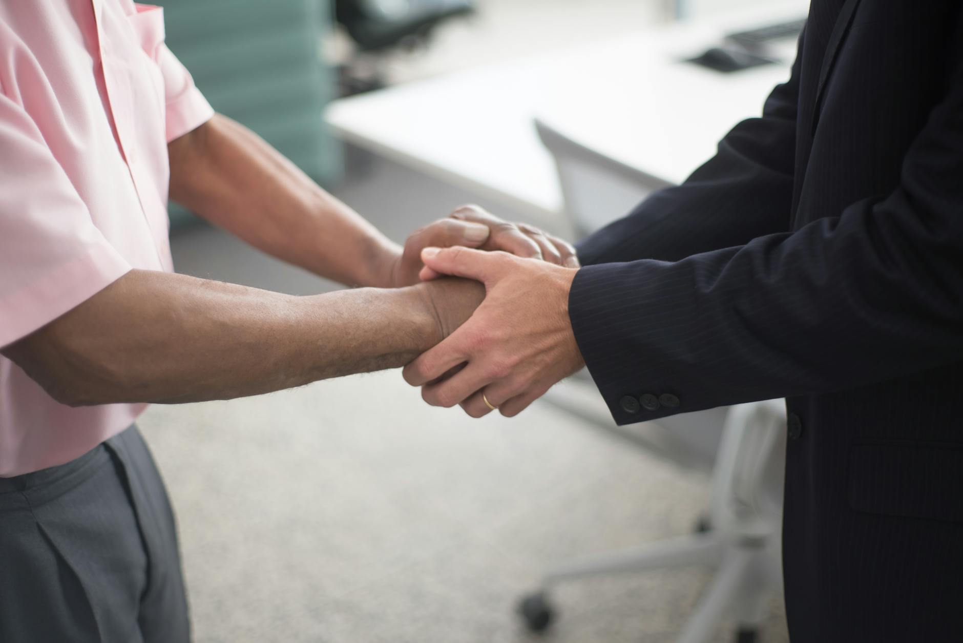 Close-up of a formal handshake between two businessmen in an office environment.