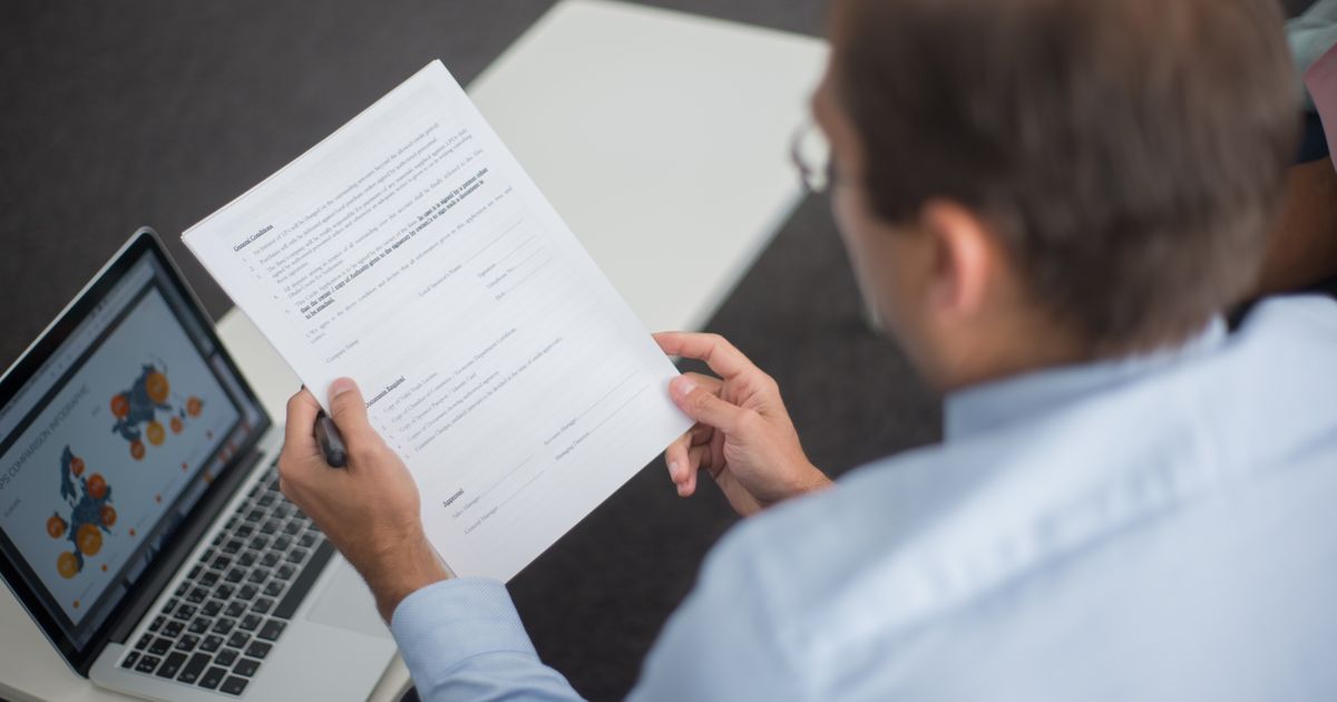 A designer reviewing a contract with charts and graphs displayed on their computer screen.