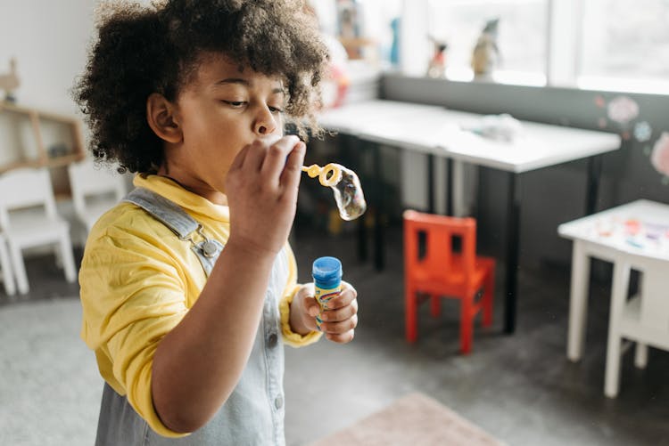 A Kid In Yellow Shirt Blowing Bubbles