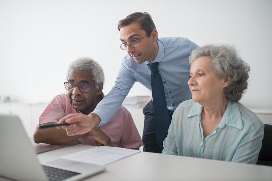 Free Insurance Agent Pointing at Laptop Screen for Elderly Clients Stock Photo