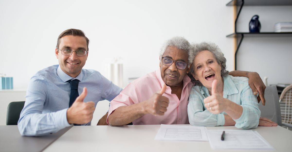 Elderly couple with consultant giving thumbs up in an office setting, showcasing positive interaction, illustrating Mature Driver Discount Car Insurance โ 1-800-MEDIGAP, America's Trusted Toll-Free Number.