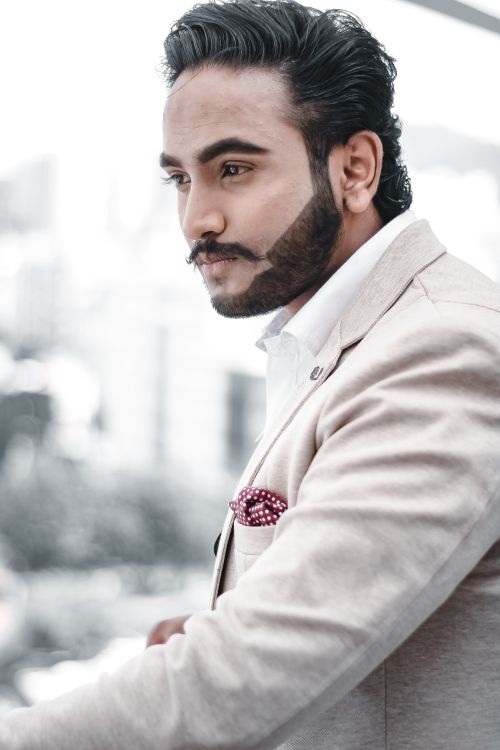 Free Portrait of a confident man in a beige suit and styled beard looking away. Light background. Stock Photo