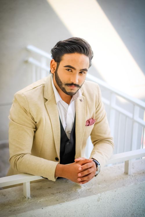 Free Well-dressed man with beard leaning on a balcony railing in a stylish suit, shot during the day. Stock Photo