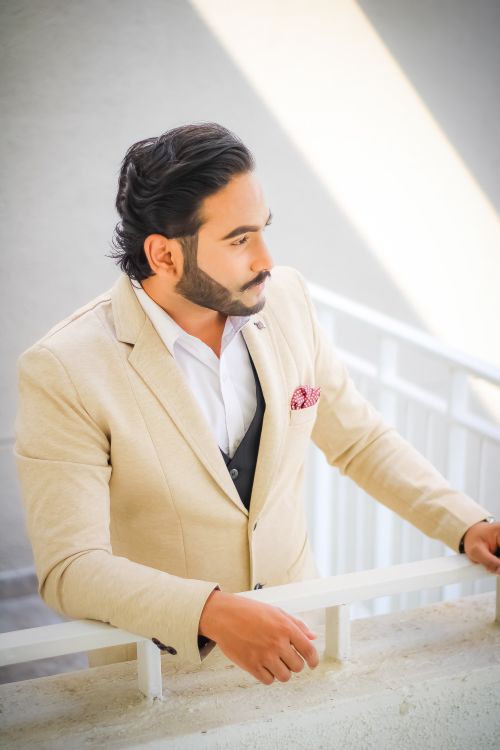 Free Elegant man in beige suit with beard leaning on balcony, exuding confidence and style. Stock Photo